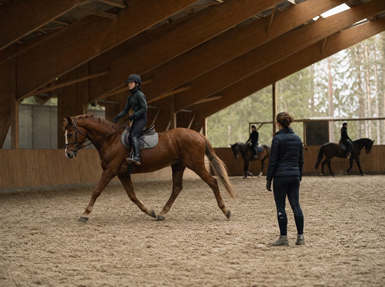Reitstunde in einer Reithalle, die Reitlehrerin beobachtet eine Schülerin im Trab